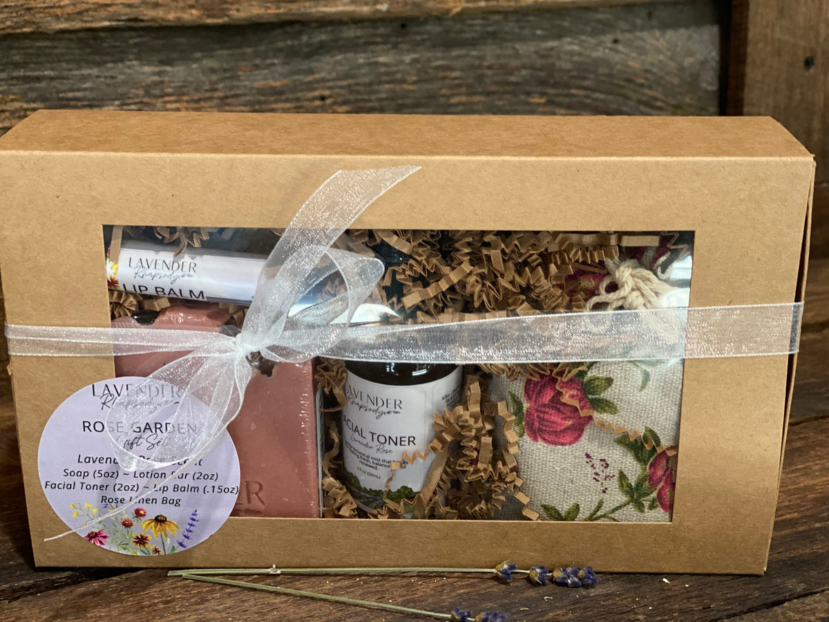 gift set in a kraft box with see through window. tied with a white ribbon.  gift set includes rose soap, passion fruit rose lip balm, lavender rose facial toner, rose print bag that includes a lavender rose lotion bar.  gift set has a sticker on front with contents of gift set.